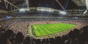 Arenans atmosfär. Storslagen vy över en fullsatt fotbollsarena där publikens jubel syns i bakgrunden när en avgörande matchmoment utförs